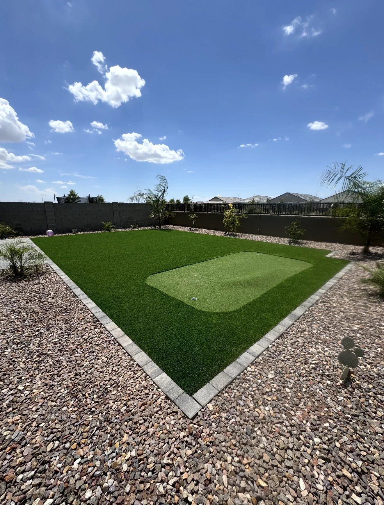 Turf lawn and backyard putting green bordered by pavers and landscape rock