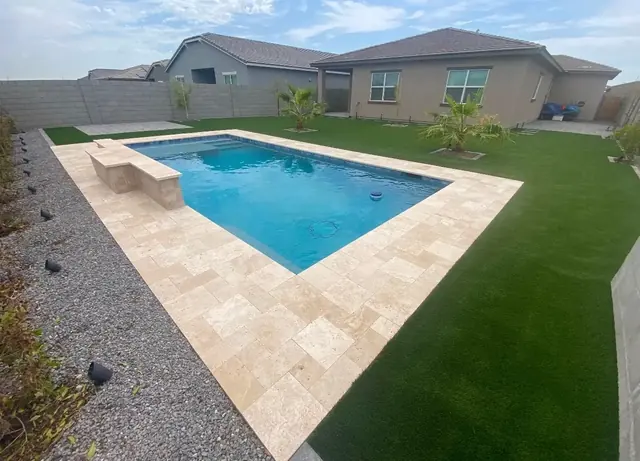 Backyard pool with a travertine deck surrounded by artificial turf