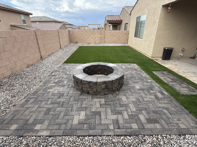 Round stone fire pit on a herringbone paver patio with artificial turf