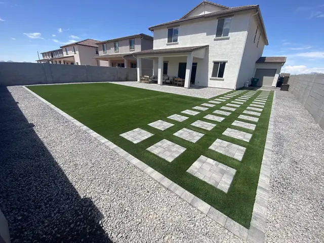 Long artificial turf lawn with paver stepping strips and rock border