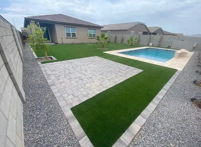 Backyard pool with a grey paver patio, artificial turf and rock