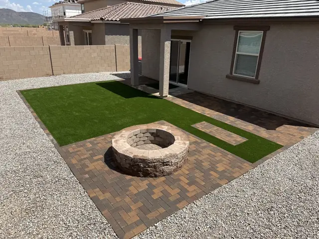 Round fire pit on warm-toned pavers beside artificial turf