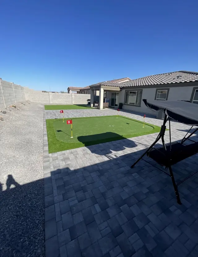 Backyard putting green beside a gray paver patio and rock landscaping