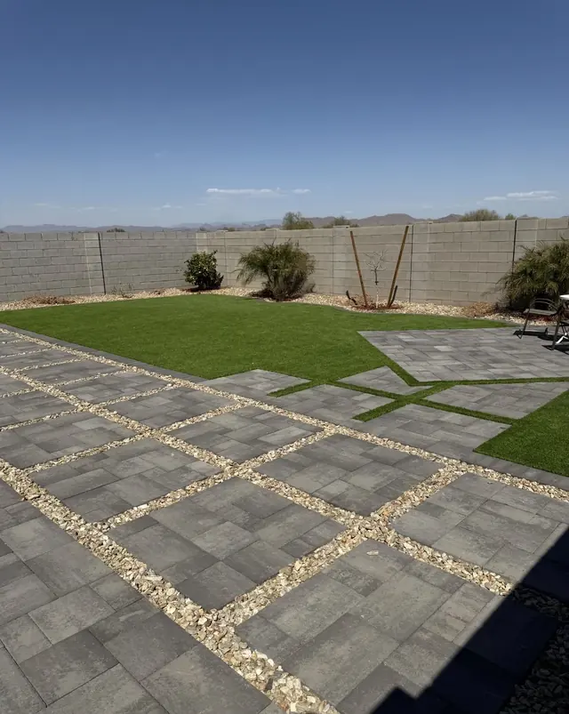 Gray paver pads separated by landscape rock beside an artificial turf lawn