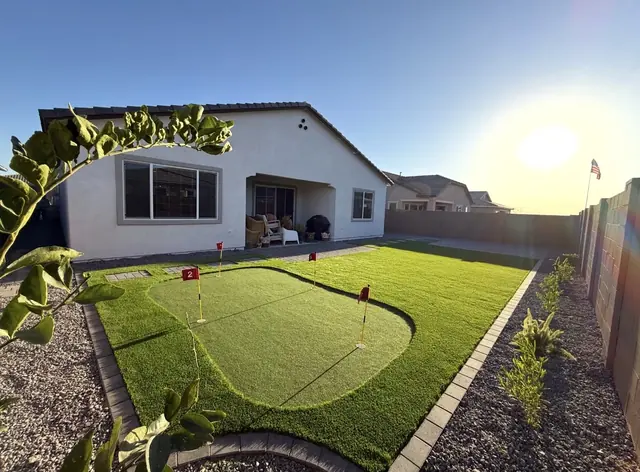 Backyard putting green in an artificial turf lawn with paver edging