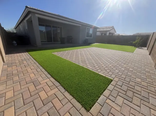 Warm-toned paver patio surrounding an artificial turf lawn