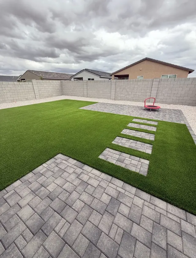 Gray paver patio with stepping pads and a broad artificial turf lawn