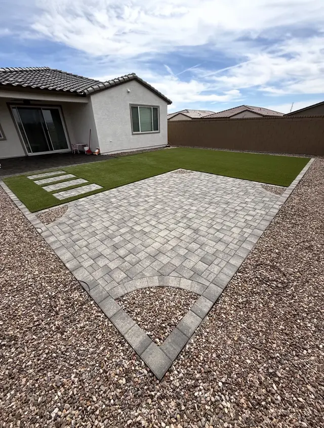 Light gray paver patio with a curved rock inset beside artificial turf