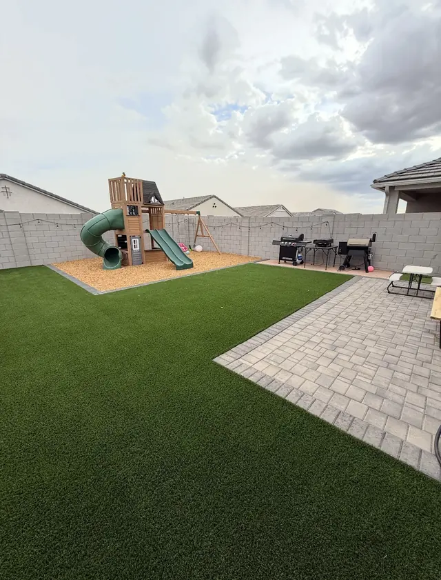 Play structure beside an artificial turf lawn and light paver patio