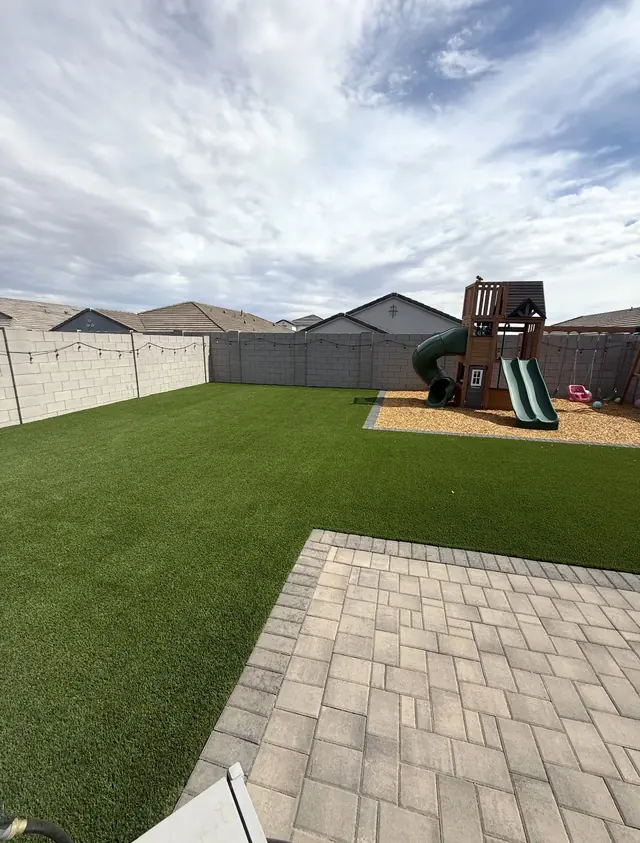 Large artificial turf lawn beside a play structure and paver patio