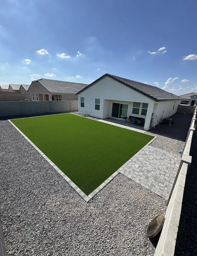 Large artificial turf lawn with a light paver patio and rock border
