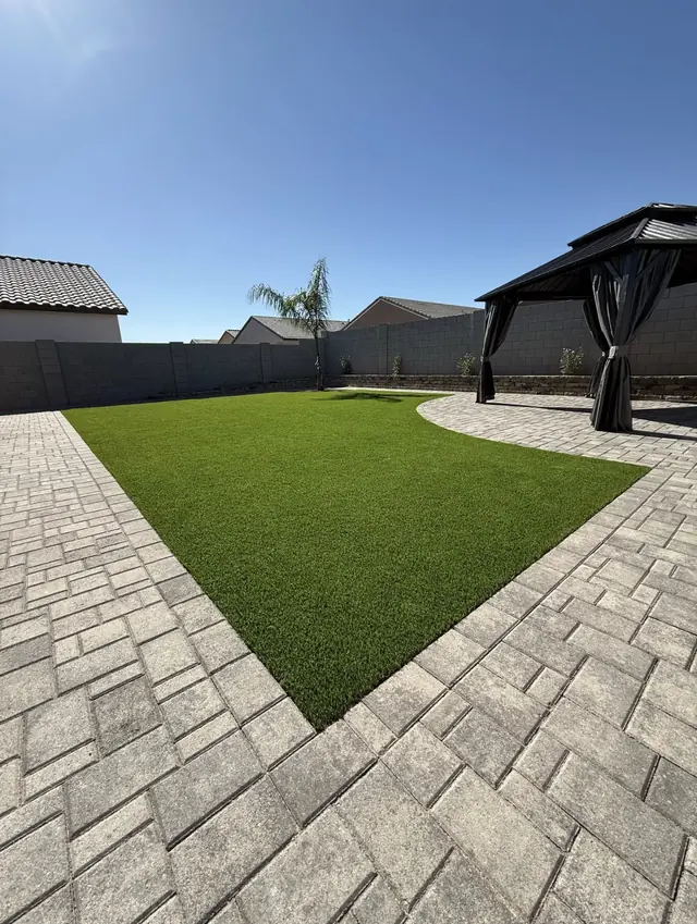 Artificial turf lawn bordered by paver patios and a shaded pavilion